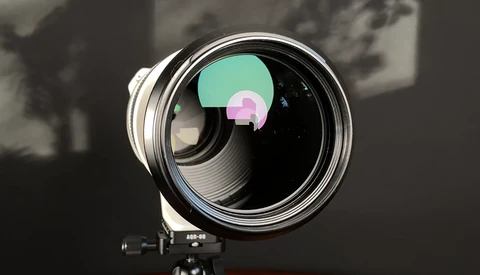 Large telephoto lens mounted on a tripod with colorful lens element visualization overlaid on the front glass.