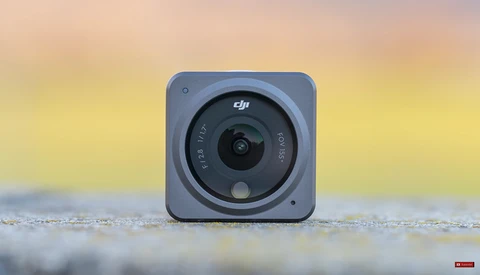DJI action camera with square body and circular lens mounted on wet surface with blurred golden sunset background.