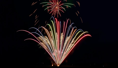 Vibrant fireworks burst across a dark night sky in red, gold, green, and white colors.
