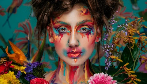 Portrait with vibrant face paint and colorful flowers surrounding the subject against a teal background.