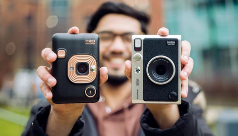 A person holding two black instant cameras with gold and silver accents side by side.