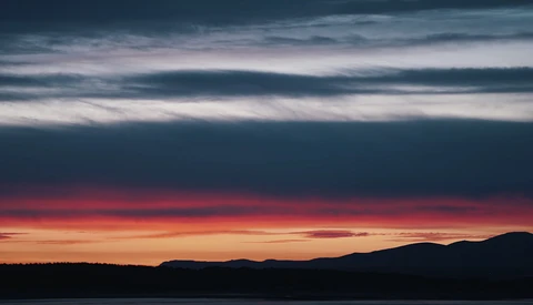 Dramatic sunset over a lake with silhouetted mountains and layered clouds in deep blue and crimson tones.