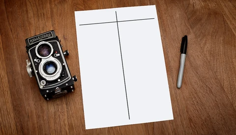 Vintage twin-lens reflex camera with blank grid-divided paper and black marker on wooden surface.