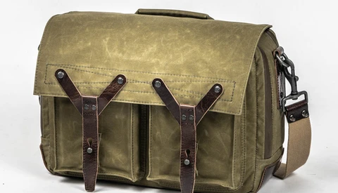 Waxed canvas messenger bag with brown leather straps and brass hardware on white background.