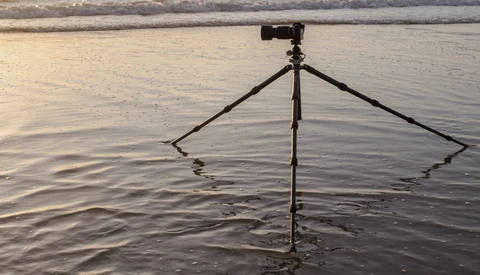 Tripod with inverted legs planted in shallow water at a beach during golden hour.