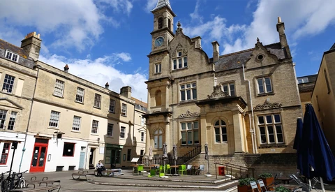 Stone Victorian building with clock tower overlooking a courtyard with contemporary seating areas.