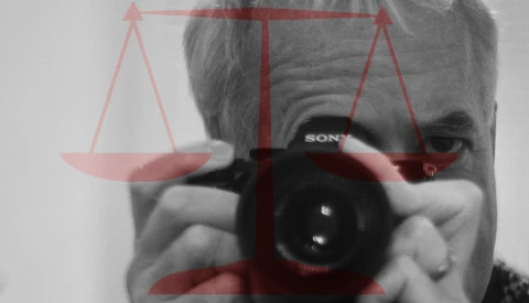 Photographer holding a Sony camera with scales of justice overlay in red and black.