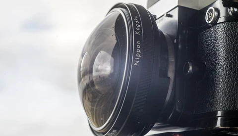 Close-up of a vintage rangefinder camera lens showing focus ring and aperture markings against overcast sky.