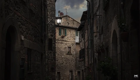 Narrow European stone alleyway with ancient buildings and distant sky visible at the end.