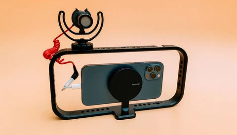 Smartphone rig setup with wireless microphone, ring light, and stabilizing frame against warm background.