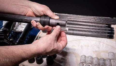 Two hands examining a wooden rifle barrel with threaded muzzle attachment during equipment inspection.