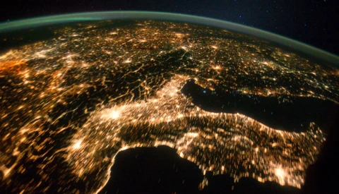 Earth at night photographed from space, showing city lights scattered across continents against a dark starry sky.