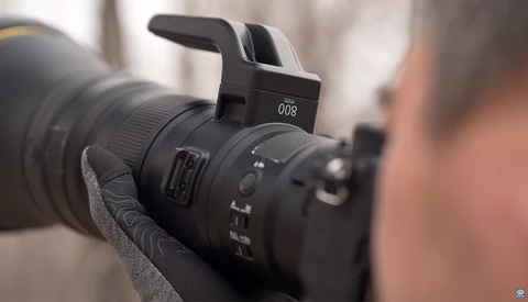 Close-up of a telephoto lens mounted on a camera with a pop-up flash positioned above the lens barrel.