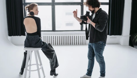 Photographer directing a model seated on a stool during a studio portrait session.