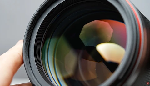 Close-up view of a camera lens barrel showing colorful optical glass elements and coatings.