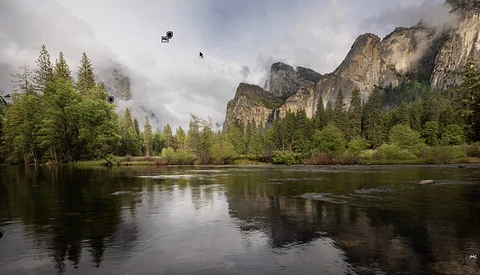 Granite cliffs rise above a calm river lined with coniferous forest, partially shrouded in mist under overcast sky.