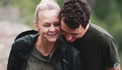 Two people embracing outdoors with blurred green foliage background.