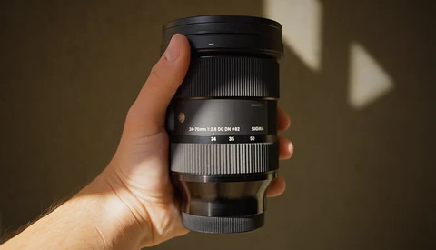 Hand holding a telephoto zoom lens with white and black barrel against a neutral background.
