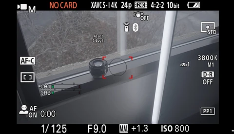 Camera LCD screen displaying manual focus assist with focus peaking overlay on a window scene.