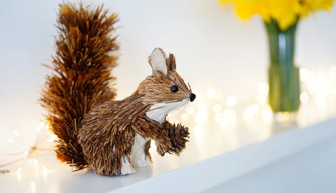 Decorative squirrel figurine crafted from twine or raffia material, photographed against a soft, bokeh background.
