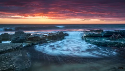 Coastal seascape at sunrise with silky water flowing around dark rocky outcrops.