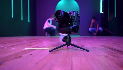 Professional camera on tripod in neon-lit studio with purple and cyan gels casting vibrant ambient light.