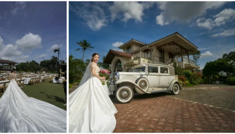 Bride in flowing white gown posing beside vintage cream-colored car in front of colonial mansion.
