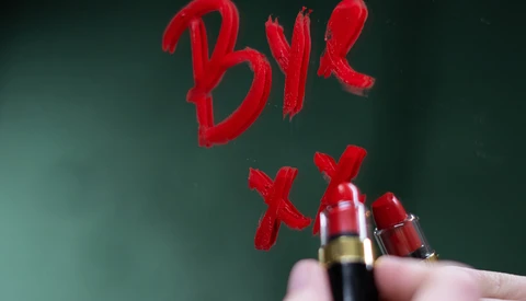 Red lipstick and cosmetic products with handwritten "BYE" text on green background.