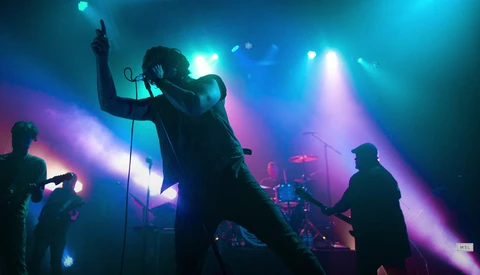 Lead singer performing center stage with microphone stand, bathed in vibrant blue and purple concert lighting.