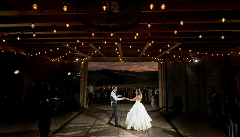 Bride and groom share their first dance under string lights in an open-air venue at dusk.