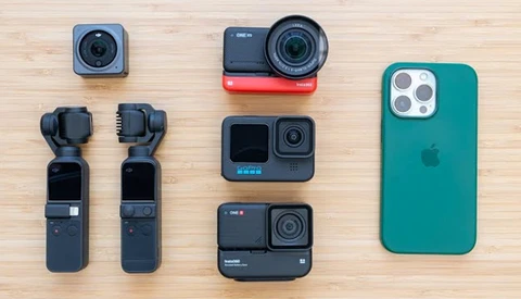 Collection of compact cameras and smartphone arranged on light wood surface.