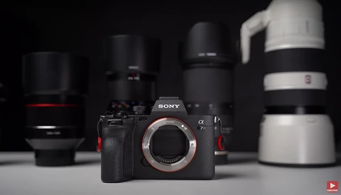 Sony α mirrorless camera body with several telephoto lenses arranged on a white surface against a dark background.