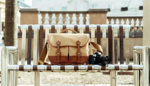 Tan and brown leather camera bag with red straps displayed on a striped beach chair next to a vintage film camera.