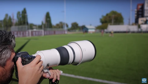 Photographer with telephoto lens photographing a soccer field during daytime.