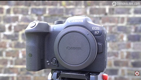 Canon EOS R7 mirrorless camera body mounted on a tripod against a brick wall background.