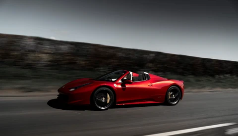Red sports car with door open, captured in motion on a curved road with blurred landscape background.