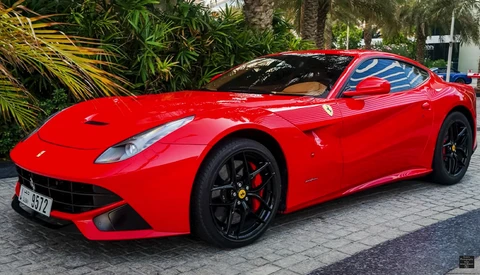 Bright red sports car with sleek coupe design parked on a paved surface surrounded by tropical vegetation.