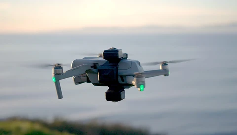 DJI Mavic drone with propellers spinning against a blurred coastal landscape at sunset.