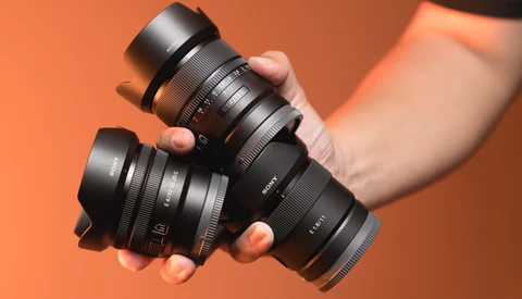 Two black camera lenses held in hands against an orange background.