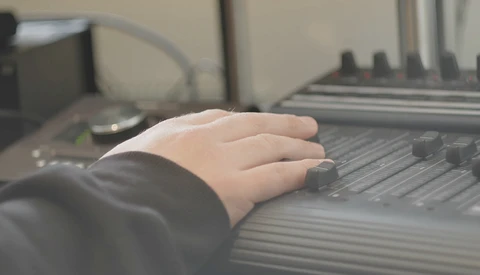 Child's hand resting on a keyboard in a home office setting with blurred computer equipment in the background.