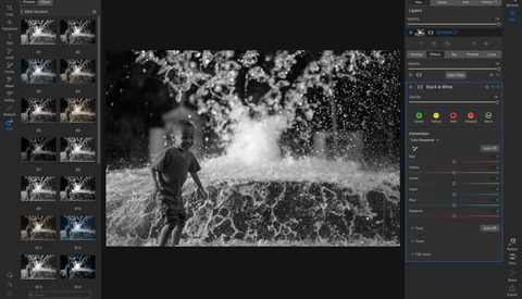 Child running through water spray in black and white photograph.