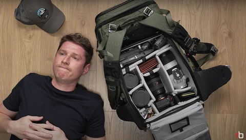 Photographer lying beside an open camera backpack displaying organized photography gear and equipment.