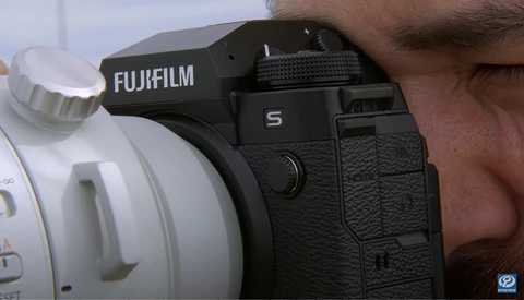 Photographer holding a Fujifilm S camera with white telephoto lens mounted.