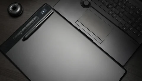 Overhead flat lay of creative workspace with graphics tablet, stylus, keyboard, and mouse on dark surface.