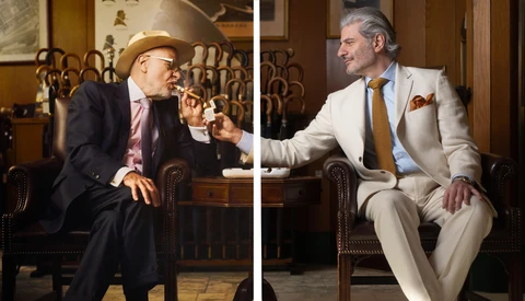 Two men in suits seated in leather chairs having a conversation in an elegant interior.