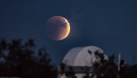 Blood moon during total lunar eclipse with warm reddish-orange glow against dark sky.