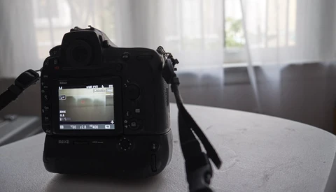 Professional DSLR camera with rear LCD screen visible, positioned on a table near a window with natural light streaming in.