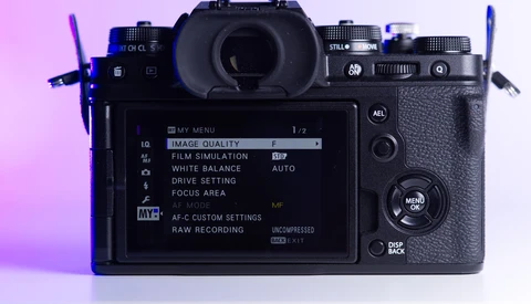 Mirrorless camera displayed from above with rear LCD screen showing menu settings against pink and purple gradient lighting.