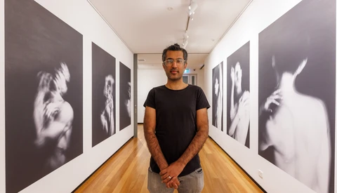 Photographer standing in gallery hallway with black and white portrait prints on both walls.