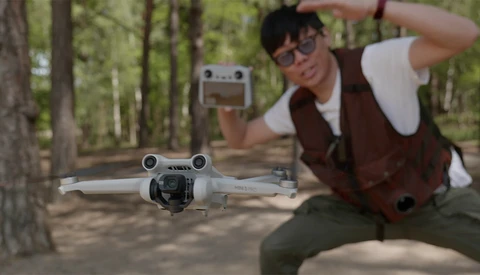 Photographer holding DJI Mini drone controller while operating a white quadcopter in a wooded area.